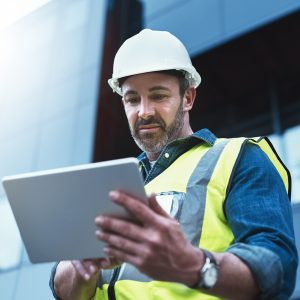 Tablet, engineer and man with helmet on construction site for development or building in city on project. Male person, tech and architecture as manager for progress in industrial, design and safety